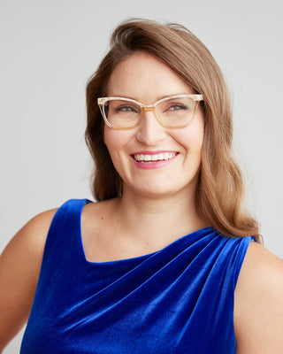 Woman wearing glasses and a blue top against a plain background. This dress is the Dewey Dress sewing pattern from Cashmerette.