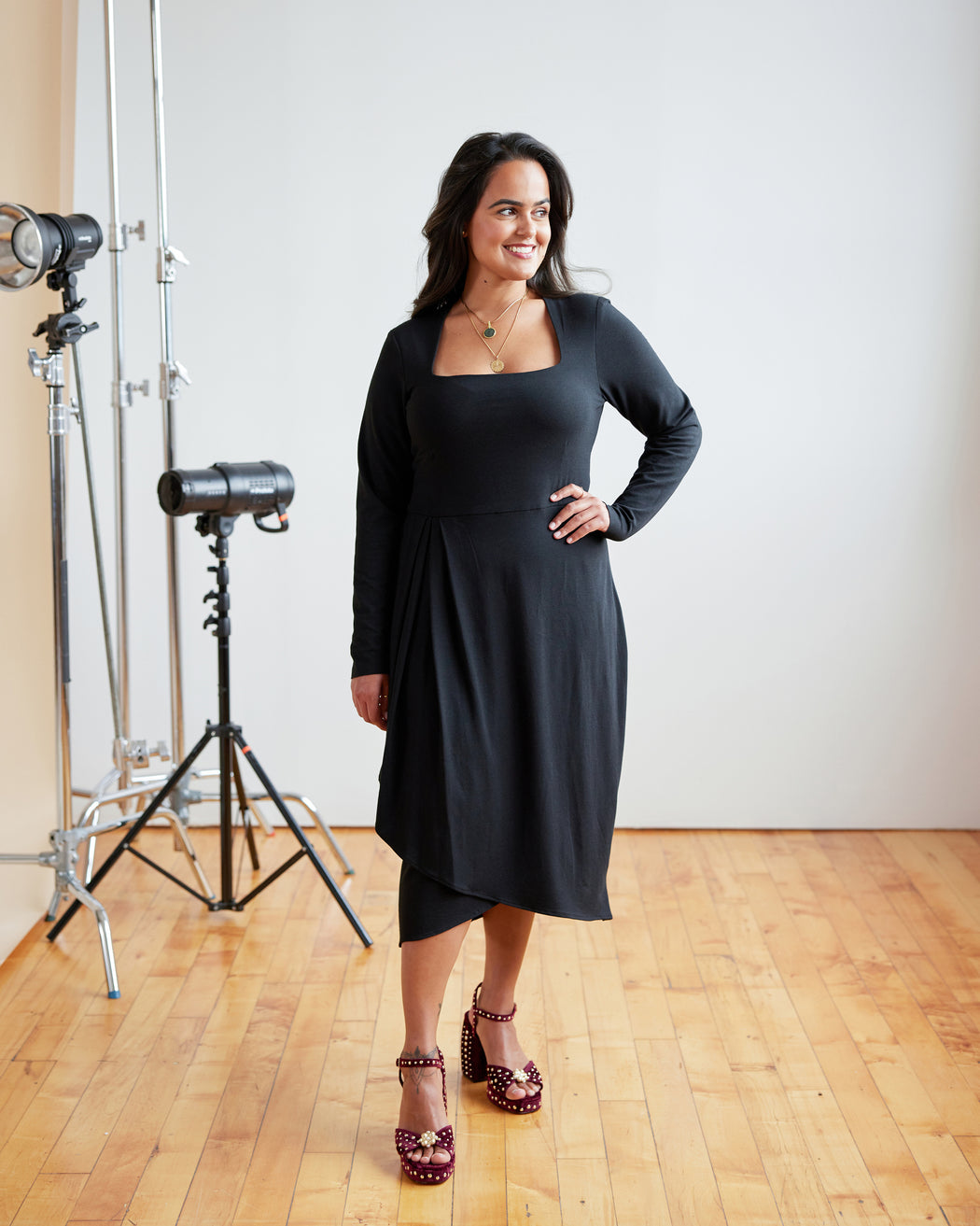 Woman in a black dress standing in a studio setting with photography equipment. This dress is the Dewey Dress sewing pattern from Cashmerette.