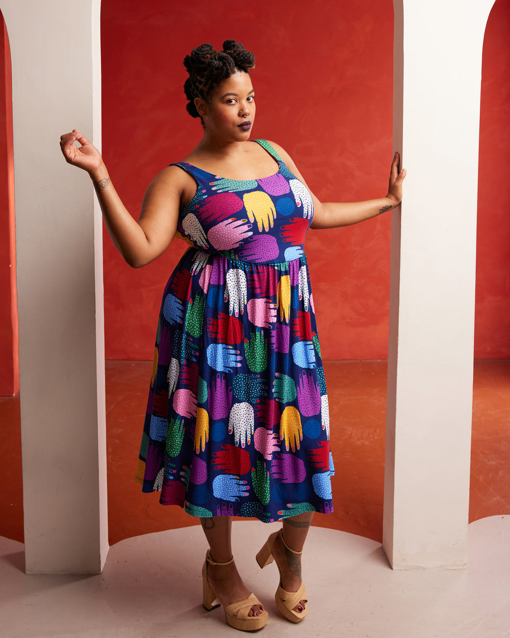 Woman wearing a colorful patterned dress against a red and white geometric background. This dress is the Irving Dress sewing pattern from Cashmerette.