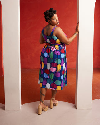 Woman wearing a colorful patterned dress against a red background. This dress is the Irving Dress sewing pattern from Cashmerette.