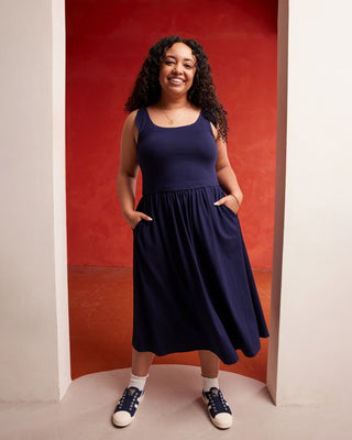 Woman wearing a navy blue dress standing against a red wall. This dress is the Irving Dress sewing pattern from Cashmerette.
