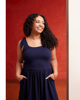 Woman wearing a navy blue dress against a red background. This dress is the Irving Dress sewing pattern from Cashmerette.