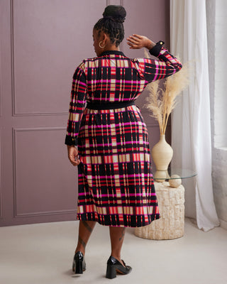 Person wearing a plaid dress in a room with a purple wall and white curtains. This is the Hazelton Wrap Dress sewing pattern from Cashmerette.