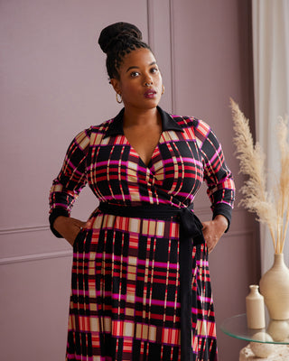 Woman wearing a colorful plaid dress standing against a pink wall. This is the Hazelton Wrap Dress sewing pattern from Cashmerette.