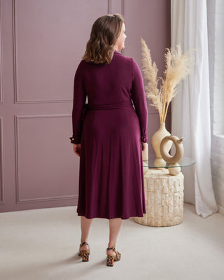 Woman in a purple dress standing in a room with a decorative vase and plants. This is the Hazelton Wrap Dress sewing pattern from Cashmerette.