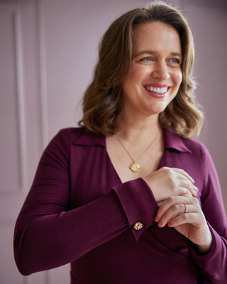 Woman wearing a purple shirt with a gold necklace and ring, standing against a plain background. This is the Hazelton Wrap Dress sewing pattern from Cashmerette.