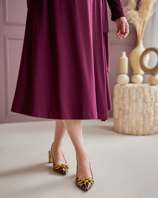 Person wearing a long burgundy dress with leopard print shoes in a room with decorative elements. This is the Hazelton Wrap Dress sewing pattern from Cashmerette.
