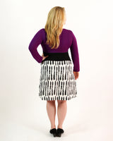 Person wearing a purple top and black and white patterned skirt on a white background. This dress is the Washington Dress sewing pattern from Cashmerette.