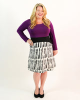 Woman wearing a purple top and black and white patterned skirt on a white background. This dress is the Washington Dress sewing pattern from Cashmerette.