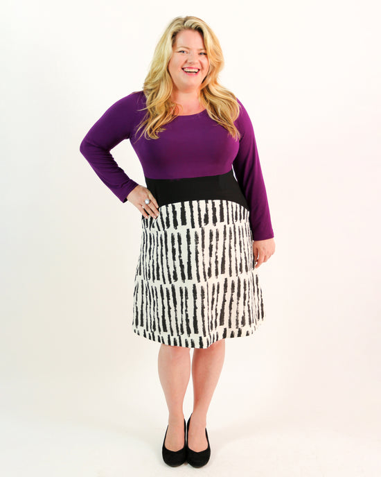 Woman wearing a purple top and black and white patterned skirt on a white background. This dress is the Washington Dress sewing pattern from Cashmerette.