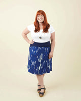 Woman wearing a white top and blue patterned skirt against a beige background. This dress is the Washington Dress sewing pattern from Cashmerette.