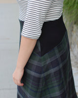 Person wearing a striped shirt and plaid skirt with a blurred background. This dress is the Washington Dress sewing pattern from Cashmerette.
