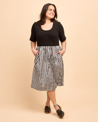 Woman wearing a black top and gingham skirt on a beige background. This is the Duxbury Dress sewing pattern from Cashmerette.