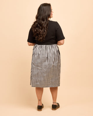 Person wearing a black top and gingham skirt on a beige background. This is the Duxbury Dress sewing pattern from Cashmerette.