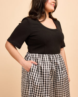 Woman wearing a black ribbed top and checkered pants against a beige background. This is the Duxbury Dress sewing pattern from Cashmerette.
