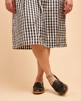 Person wearing a black and white checkered dress with brown sandals on a beige background. This is the Duxbury Dress sewing pattern from Cashmerette.