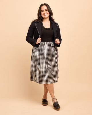 Woman wearing a black jacket, black top, and checkered skirt on a beige background. This is the Duxbury Dress sewing pattern from Cashmerette.