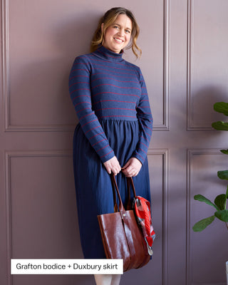 Woman wearing a blue dress holding a brown bag against a purple paneled wall. This is the Duxbury Dress sewing pattern from Cashmerette. Over the image is the text "Grafton bodice + Duxbury skirt"