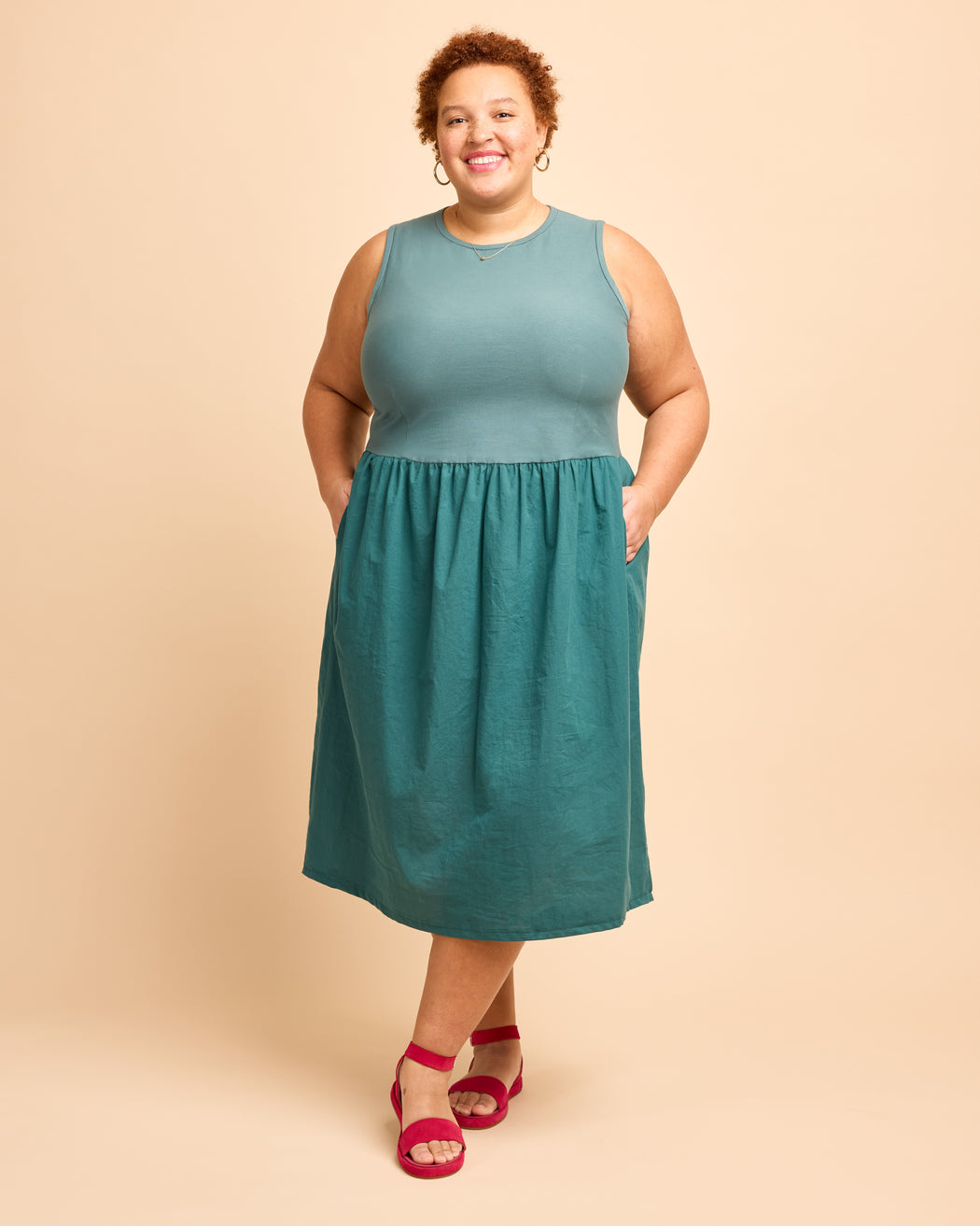 Woman wearing a teal dress on a beige background. This is the Duxbury Dress sewing pattern from Cashmerette.