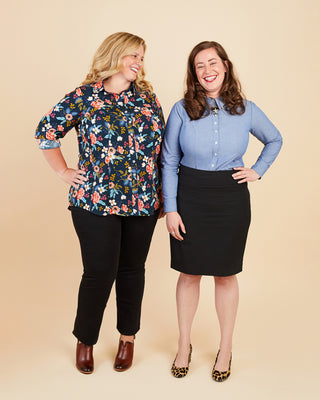 Two women standing side by side against a beige background, wearing colorful shirts and black pants.. This button-up shirt is the Harrison Shirt sewing pattern from Cashmerette.
