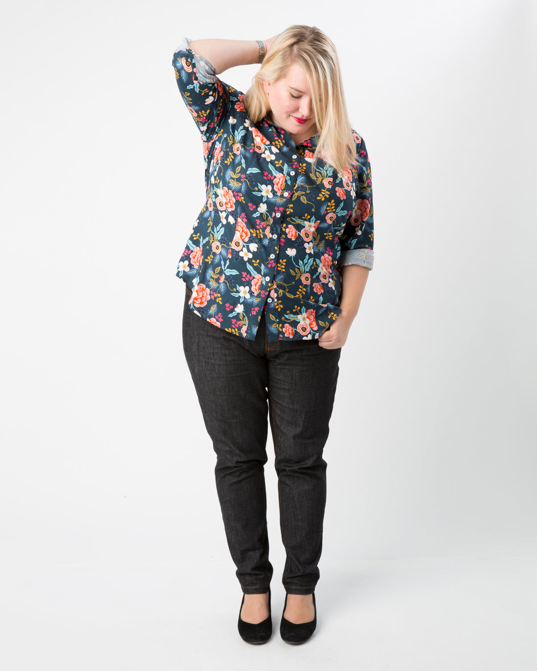 Woman wearing a floral blouse and black pants on a white background. This button-up shirt is the Harrison Shirt sewing pattern from Cashmerette.
