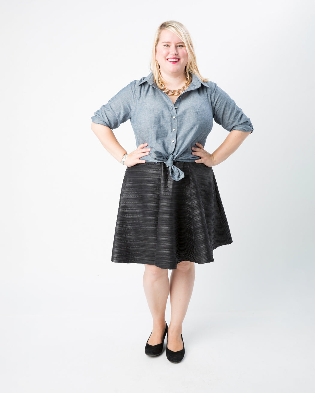 Woman wearing a blue shirt and black skirt on a white background. This button-up shirt is the Harrison Shirt sewing pattern from Cashmerette.