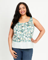 Woman wearing a floral sleeveless top with a plain white bottom on a light gray background. This top is the Springfield Top sewing pattern from Cashmerette.