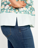 Person wearing a floral blouse and blue jeans on a white background. This top is the Springfield Top sewing pattern from Cashmerette.