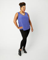 Woman wearing a purple sleeveless top and black leggings on a white background. This top is the Webster Dress & Tunic sewing pattern from Cashmerette.