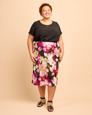 Woman wearing a black top and floral skirt on a beige background. This is the Montrose Top sewing pattern from Cashmerette.