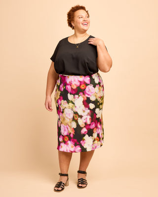 Woman wearing a black top and floral skirt on a beige background. This is the Montrose Top sewing pattern from Cashmerette.