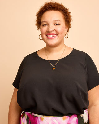 Woman wearing a black top with floral pants against a beige background. This is the Montrose Top sewing pattern from Cashmerette.