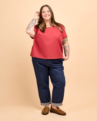Woman wearing a red top and blue jeans on a beige background. This is the Montrose Top sewing pattern from Cashmerette.