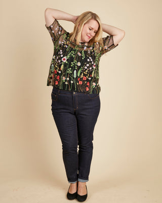 Woman wearing a floral top and dark jeans against a beige background. This top is the Montrose Top sewing pattern from Cashmerette.