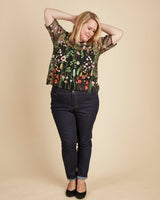 Woman wearing a floral top and dark jeans against a beige background. This top is the Montrose Top sewing pattern from Cashmerette.
