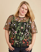 Woman wearing a black floral embroidered top against a beige background. This top is the Montrose Top sewing pattern from Cashmerette.