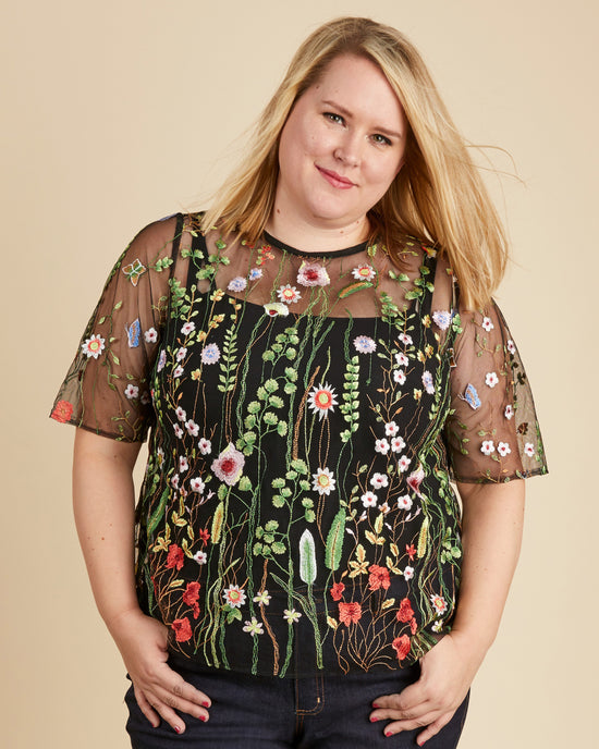 Woman wearing a black floral embroidered top against a beige background. This top is the Montrose Top sewing pattern from Cashmerette.