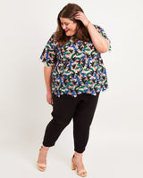 Woman wearing a floral blouse and black pants on a white background. This top is the Montrose Top sewing pattern from Cashmerette.
