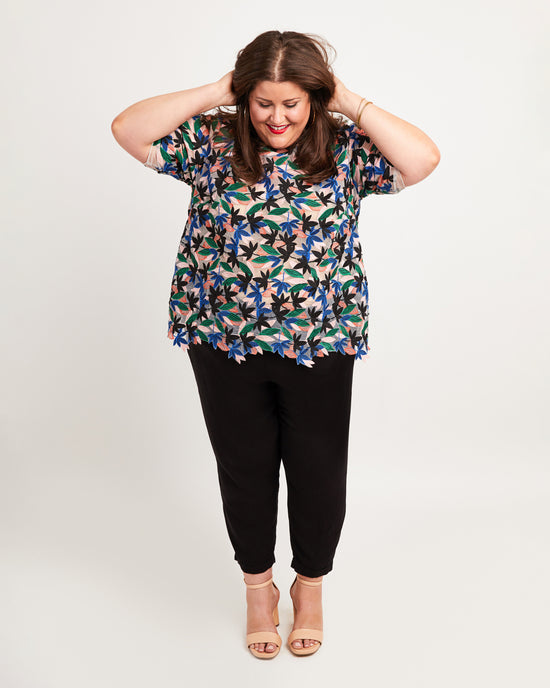 Woman wearing a floral blouse and black pants on a plain background. This top is the Montrose Top sewing pattern from Cashmerette.
