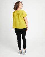 Woman wearing a yellow top and black pants on a white background. This top is the Montrose Top sewing pattern from Cashmerette.