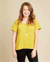 Woman wearing a yellow shirt and black pants against a beige background. This top is the Montrose Top sewing pattern from Cashmerette.