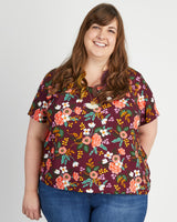 Woman wearing a floral blouse with a plain background. This top is the Montrose Top sewing pattern from Cashmerette.