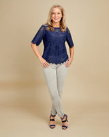 Woman wearing a blue lace top and light gray pants on a beige background. This top is the Montrose Top sewing pattern from Cashmerette.