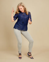 Woman wearing a blue lace top and light gray pants on a beige background. This top is the Montrose Top sewing pattern from Cashmerette.