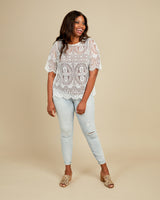 Woman wearing a patterned top and light blue jeans on a beige background. This top is the Montrose Top sewing pattern from Cashmerette.