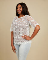 Woman wearing a white lace top against a beige background. This top is the Montrose Top sewing pattern from Cashmerette.