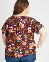 Woman wearing a floral patterned top on a plain background. This top is the Montrose Top sewing pattern from Cashmerette.