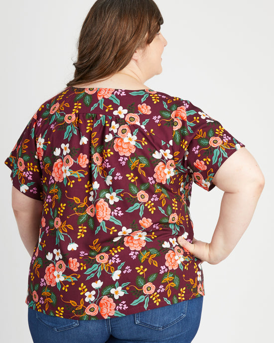 Woman wearing a floral patterned top on a plain background. This top is the Montrose Top sewing pattern from Cashmerette.