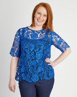 Woman wearing a blue lace top against a plain background. This top is the Montrose Top sewing pattern from Cashmerette.