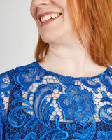 Close-up of a person wearing a blue lace dress with a plain background. This top is the Montrose Top sewing pattern from Cashmerette.